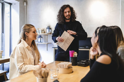 Waiter talking with female customers while taking order in restaurant