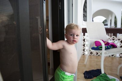 Chubby toddler boy walks out of screen door, camera aware