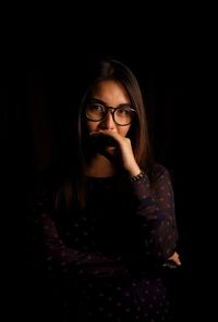 Portrait of young woman standing against black background