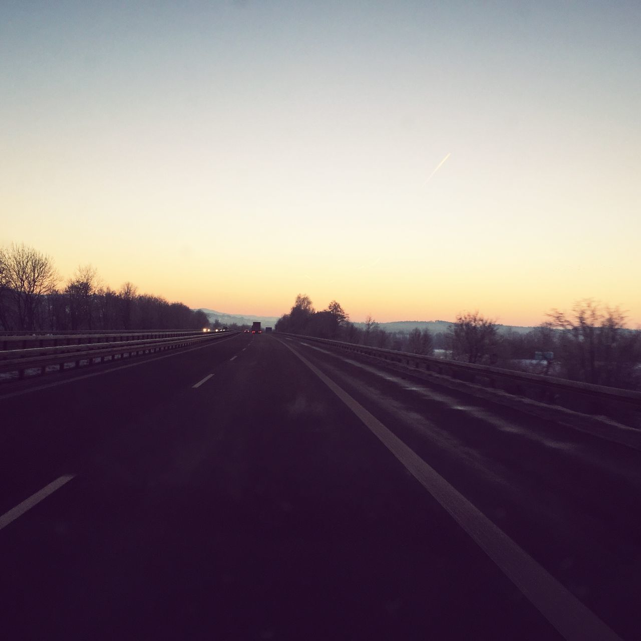 ROAD AMIDST TREES AGAINST CLEAR SKY AT SUNSET