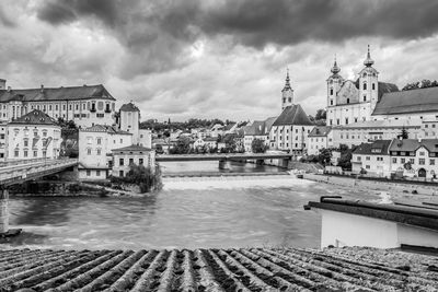 View of city by river against cloudy sky