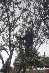 Low angle view of woman standing by trees against sky