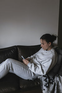 Young woman sitting on sofa and using cell phone
