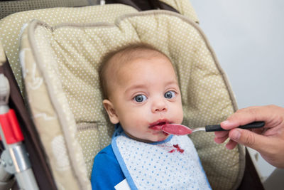 Cropped woman feeding baby boy on baby carriage at home