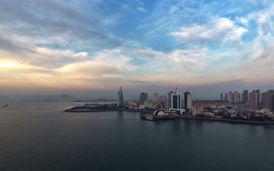 View of city at waterfront against cloudy sky