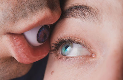 Close-up of woman looking at boyfriend holding artificial eyeball in mouth