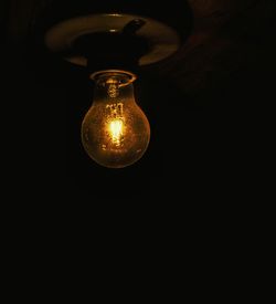 Low angle view of illuminated light bulb against black background