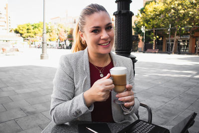 Portrait of smiling young woman holding drink in city