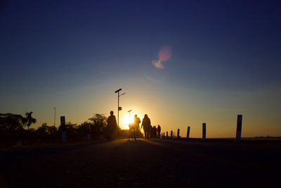 Silhouette people on street against sky during sunset
