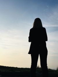 Rear view of silhouette woman standing on field against sky