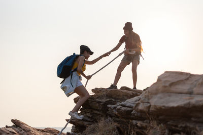 Low angle view of woman climbing on rock against sky