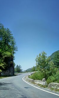 Empty road amidst trees against clear blue sky