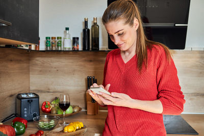 A young girl stands in the kitchen and is distracted from cooking by talking on a mobile phone 