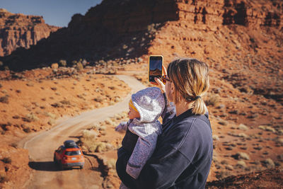 Man photographing woman on rock