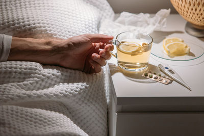 Sick man laying in bed, hold cup of hot tea with lemon. male drinking hot beverage influenza season.
