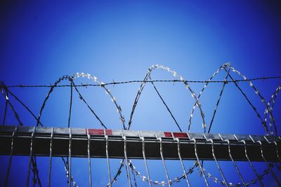 Low angle view of barbed wire against clear blue sky