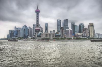 Modern buildings by river against cloudy sky