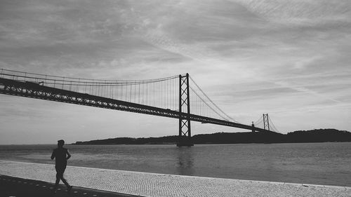 Rear view of man running on promenade against april 25th bridge over tagus river