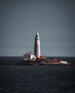 Lighthouse by sea against clear sky