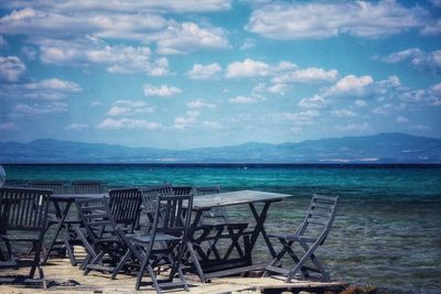 Empty chairs on beach against sky
