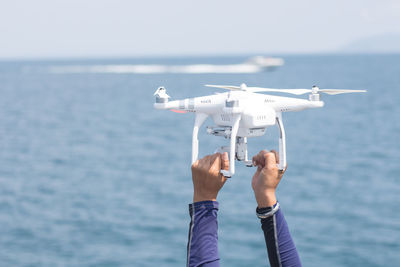 Cropped hands of man holding drone against sea