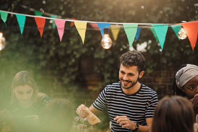 Smiling young man enjoying dinner party with friends in backyard