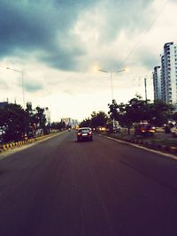 Road passing through city against cloudy sky