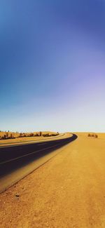 Road by land against clear blue sky