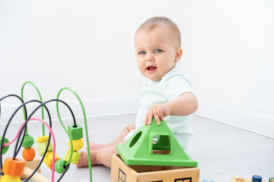 Portrait of cute boy playing with toys on floor against white background