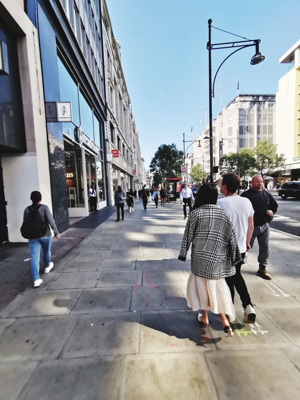 REAR VIEW OF PEOPLE WALKING ON FOOTPATH AGAINST BUILDINGS