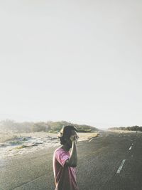 Woman photographing on mobile phone on landscape against clear sky