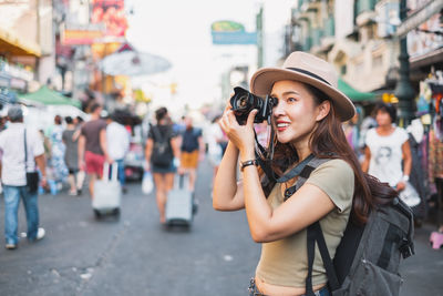 Young woman photographing while standing on street in city