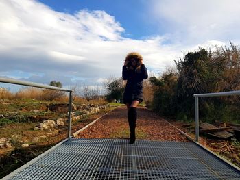 Rear view of woman standing by railing against sky