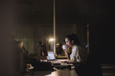 Businesswoman drinking coffee while working overtime in office at night