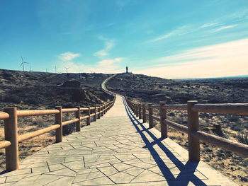 Empty footpath leading to bridge against sky