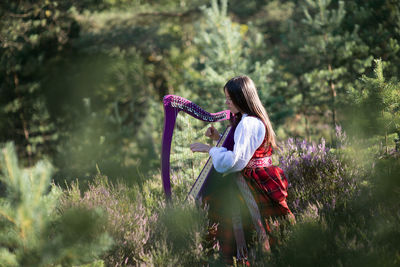 Woman playing harp against trees in forest