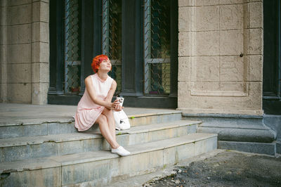 Young woman holding disposable cup while sitting on steps