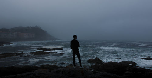 Rear view of man standing at beach against clear sky