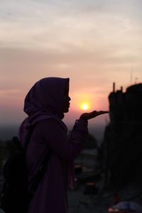 Side view of silhouette man standing against sky during sunset