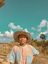 Portrait of boy wearing hat standing on field against sky