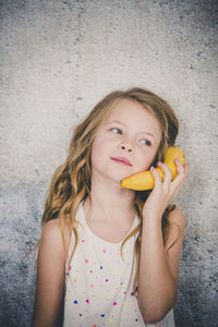 Close-up of girl holding banana against wall