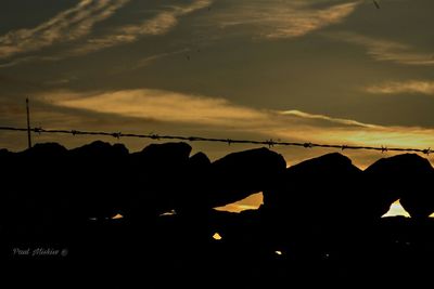 Silhouette hanging light against sky at sunset