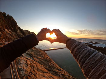 Couple making heart shape against sea and sky