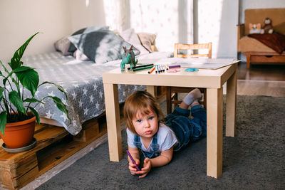 Little child playing hide and seek at home under the children's table.