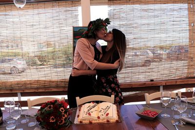 Lesbian couple kissing while standing by window during celebration