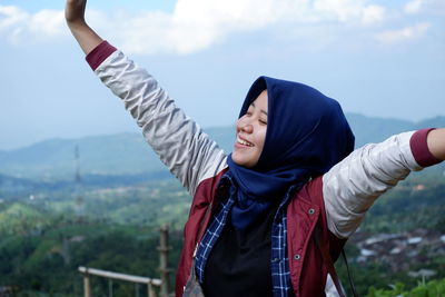 Rear view of woman with arms raised standing against sky