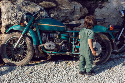 Child boy in a green jumpsuit walks among old motorcycle in the summer