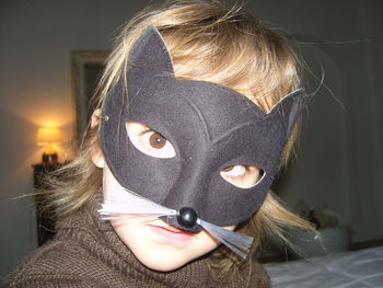 Close-up portrait of girl wearing cat mask at home