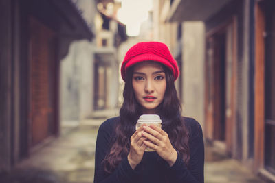 Portrait of young woman having coffee while standing in city