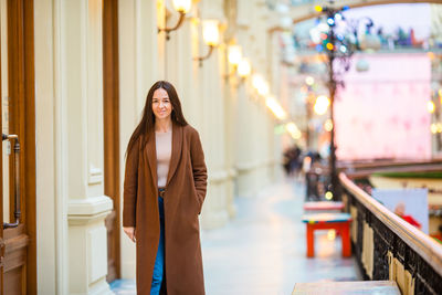 Portrait of woman standing on footpath by building